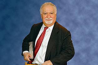 Portrait of Vartan Gregorian, distinguished educator and former president of Carnegie Corporation of New York, standing with a book in hand and wearing a suit and tie.