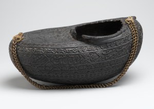 A Beggar's Bowl Kashkūl, or Beggar’s Bowl, with Portrait of Dervishes and a Mounted Falconer. Iran, A.H. 1280/1880 C.E. Coco-de-mer shell and chain. Brooklyn Museum, Henry L. Batterman Fund, 47.203.5. Kashkūls carried the donations on which dervishes relied for sustenance and also functioned as drinking vessels or food containers for wandering ascetics. They simultaneously symbolized the emptying of the Sufi’s soul or ego through the renunciation of worldly goods and aspirations, and the nourishment of that soul with divine knowledge. Many kashkūls bear inscriptions invoking God, the house of the prophet Muhammad, or the twelve Shiʿa imams. The bowls were produced in a variety of media and were held or hung from the shoulder by metal chains. The earliest examples date to the thirteenth or fourteenth century, but their form may have been derived from crescent- and boat-shaped wine bowls made in pre-Islamic Iran. This example was made from the nutshell of the coco-de-mer palm native to islands of the Indian Ocean. The shells’ lengthy sea voyage to the shores of Iran carries special significance as a metaphor for the Sufi’s mystical journey. It includes a portrait of dervishes with tamed cats and two small kashkūls. Verses of Persian mystical poetry have been engraved into the rim (see below)