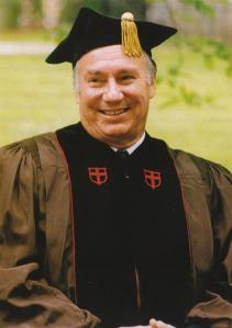 His Highness Prince Karim Aga Khan IV wearing an academic gown with a graduation cap, smiling outdoors.