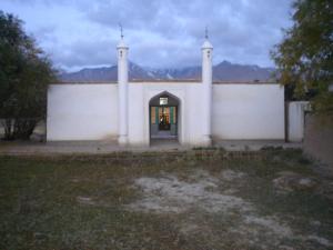 Exterior view of a Jamatkhana building with two minarets, set against a mountain backdrop during twilight.