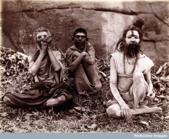 Two men and a boy sitting cross-legged on the ground surrounded by leaves; their faces are painted white and one of them appears to be smoking a pipe: Bombay at the time of the 1896/97 plague. Photo Credit: Wellcome Library, London. Wellcome Images.