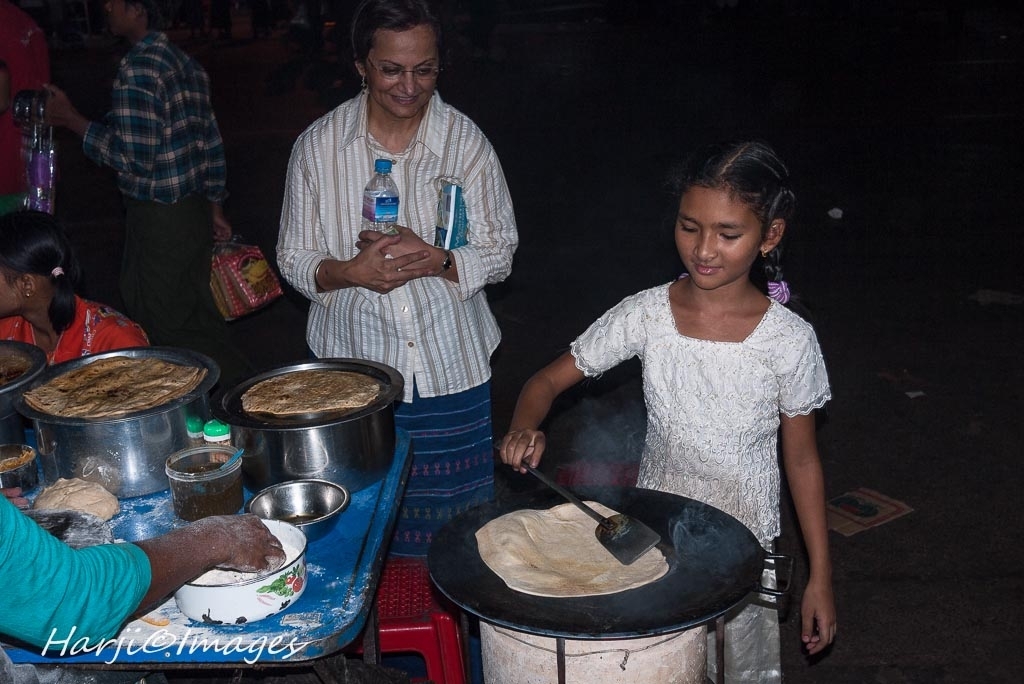 Nevin Harji looks on as a smiling young Burmese girl prepares hot roti/paratha. Please click on photo for "Street Foods of South Asia. Photo: Muslim Harji, Montreal, PQ, Canada. Copyright. 