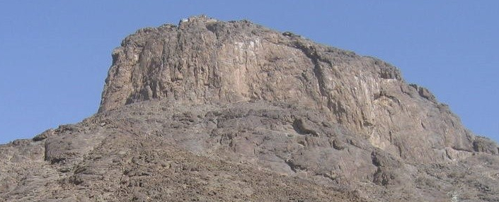 A close-up view of Mount Hira, a rocky mountain with a sheer face under a clear blue sky.