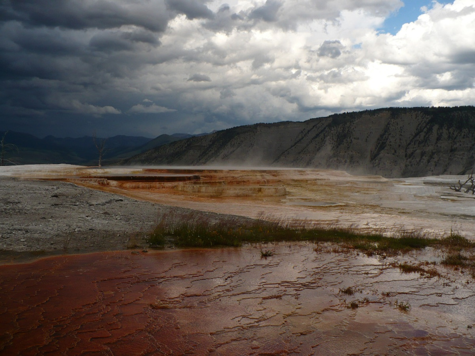 A scenic view of Yellowstone National Park featuring colorful geothermal formations and a cloudy sky.
