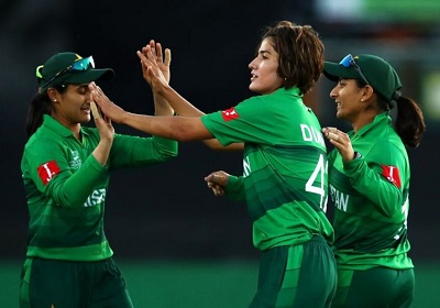 Three female cricketers in green uniforms celebrating a wicket during a match.