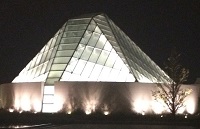 A night view of the Ismaili Centre with its distinctive glass dome, illuminated warmly against a dark sky.