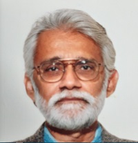 A portrait of an elderly man with gray hair and a beard, wearing glasses and a formal jacket, looking directly at the camera.