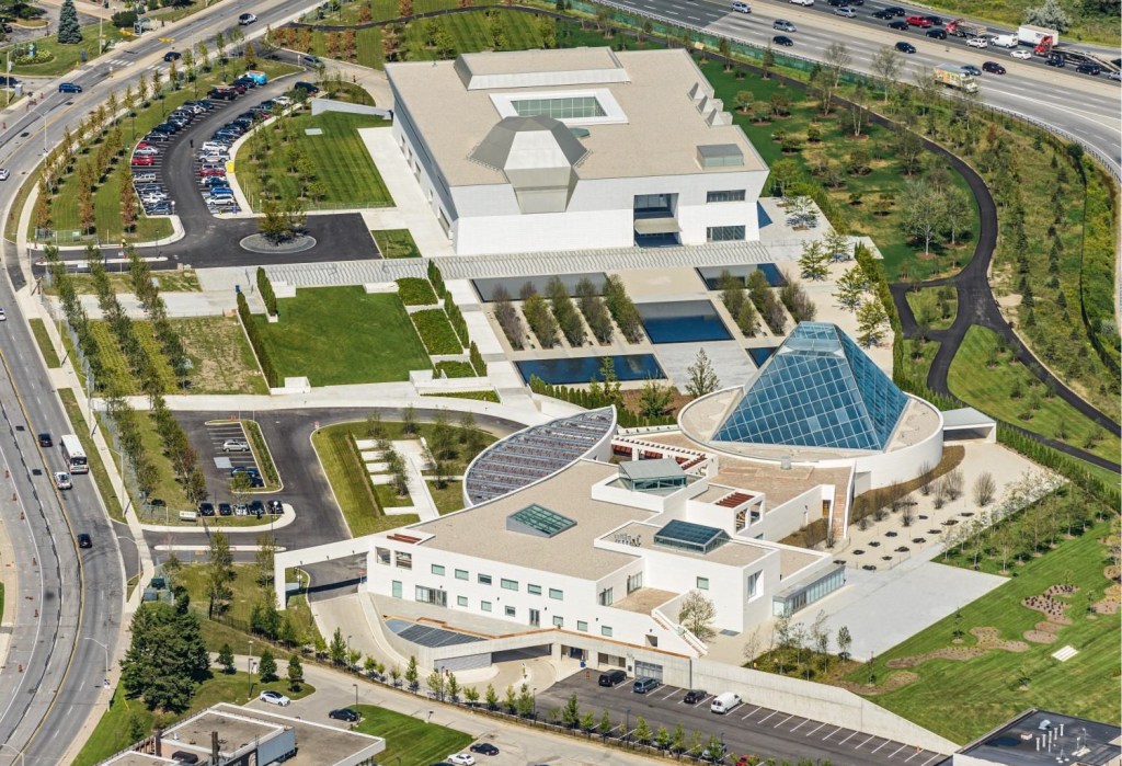 Aerial view of the Aga Khan Museum and Ismaili Centre in Toronto, showcasing modern architectural design, landscaped grounds, and surrounding parking areas.