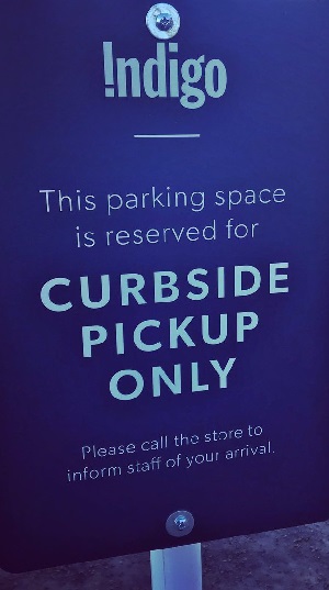 Sign indicating a parking space reserved for curbside pickup at Indigo bookstore, with instructions to call the store upon arrival.