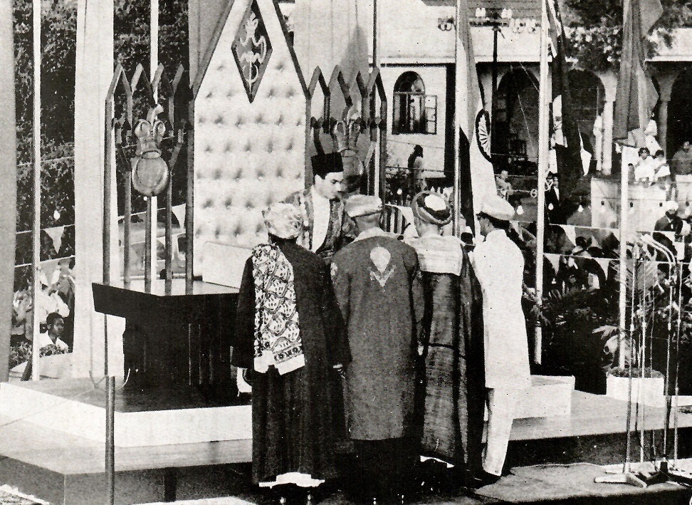 A historical photograph of a ceremonial installation event featuring a group of individuals gathered around a prominent figure at an ornate platform, with flags and decorations in the background.