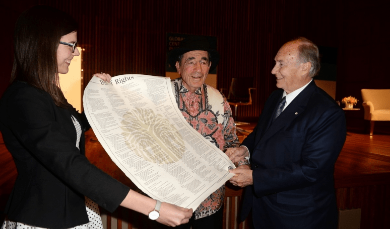 A woman and two men engage in a conversation while holding a large document titled 'Bill of Rights' in a formal setting.