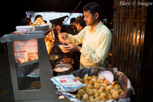 A street vendor serving traditional street food, with a display of round, crispy snacks in a basket.