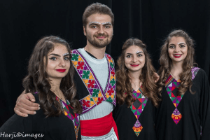 A group portrait of a young man and three young women dressed in traditional attire, showcasing colorful patterns, with a dark background.