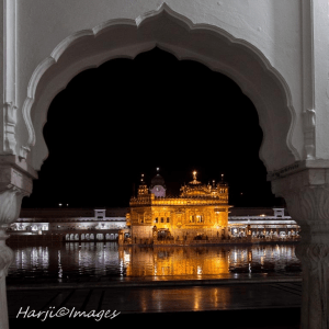 A night view of the Golden Temple, illuminated and reflecting in the surrounding water, framed by an ornate archway.