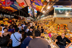 A bustling marketplace filled with colorful stalls displaying a variety of fruits, sweets, and snacks, crowded with people exploring the vibrant offerings.