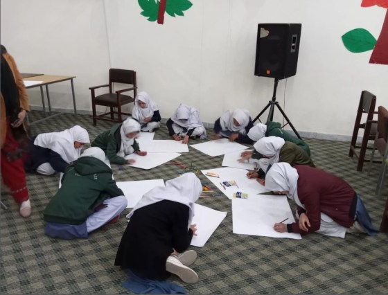 A group of children in school uniforms sitting on the floor, engaged in an art activity while drawing and coloring on large sheets of paper.
