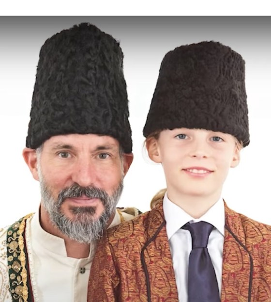 A man and a boy wearing traditional hats and formal attire, smiling for the camera.