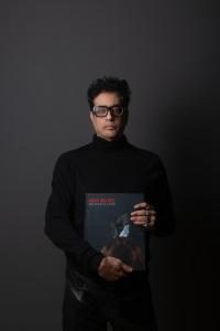 Amin Gulgee holding his monograph 'No Man's Land' against a dark background.