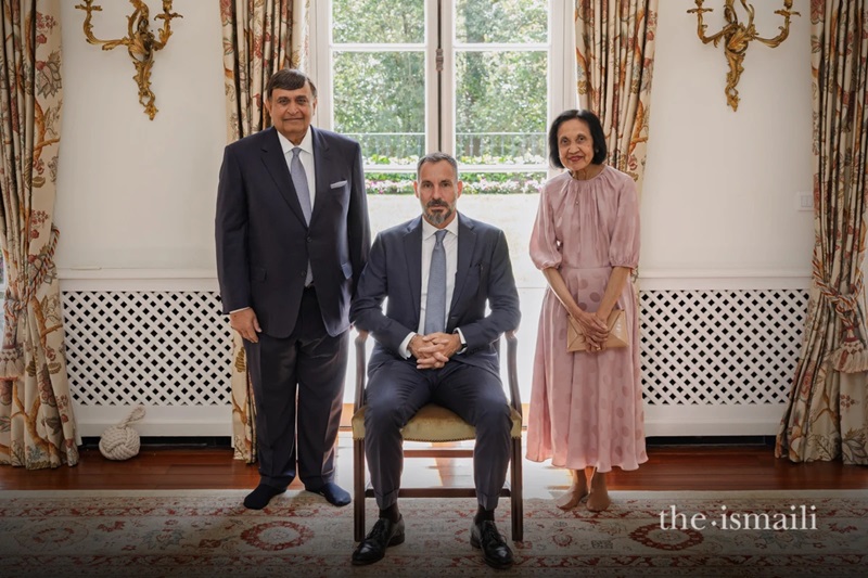Group portrait of Shafik Sachedina, seated in the center, flanked by two other individuals, with a large window in the background. The setting appears to be a well-decorated interior space.