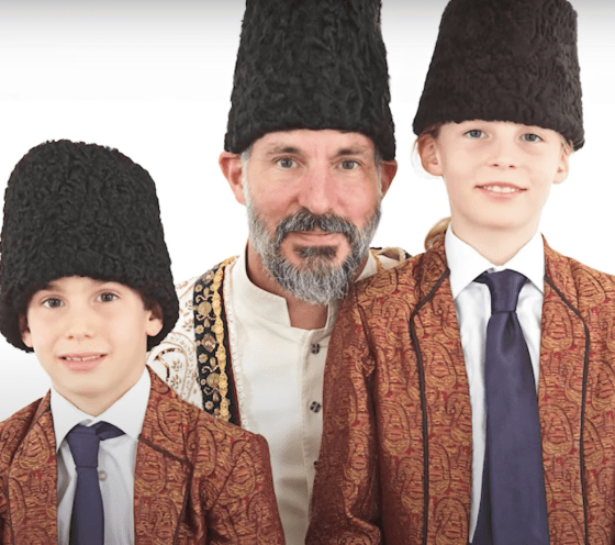 A man and two boys wearing traditional attire and hats pose together for a photo, likely celebrating a cultural or religious event.