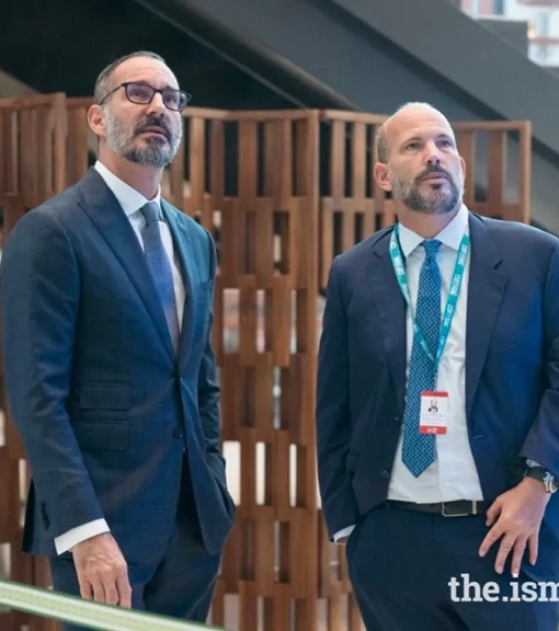 Two men in business attire looking up, with a modern wooden structure in the background.